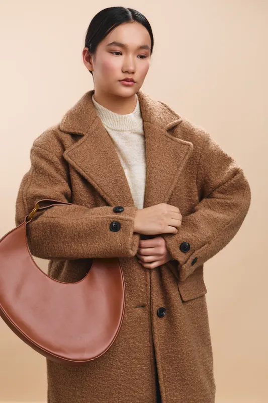 asian woman wearing a wool coat poses for a studio portrait with a neutral backdrop. she appears calm and confident, presenting a refined and stylish look.