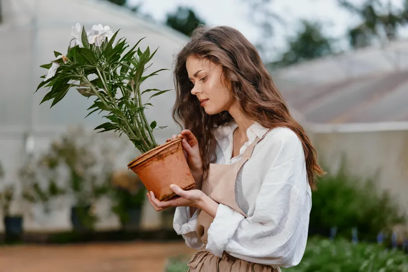 Young woman in a greenhouse caring for a potted plant, showcasing a passion for gardening and nature s beauty in a serene, natural environment