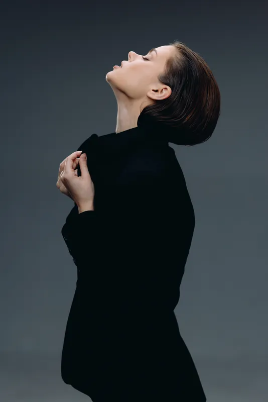 Elegant woman in black turtleneck posing with closed eyes against gray background, showcasing grace and calmness.