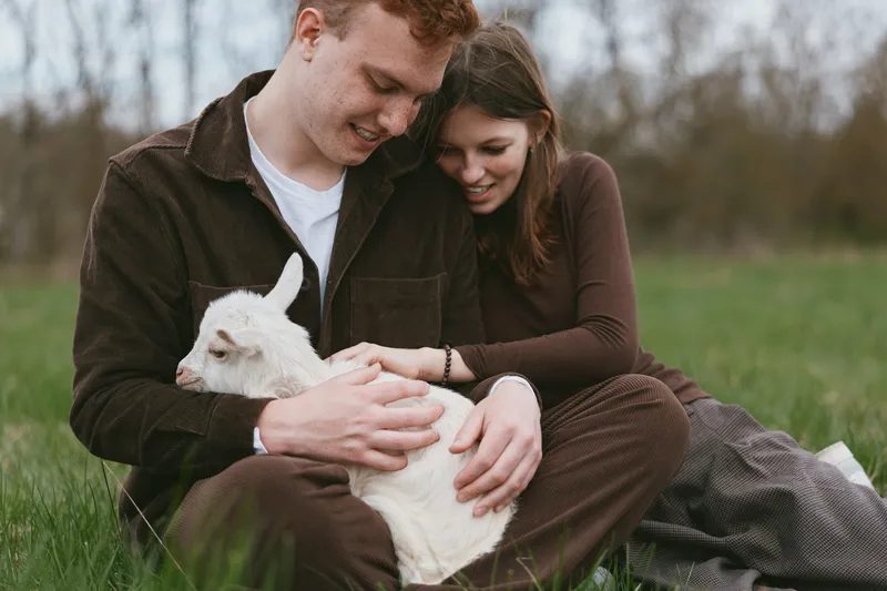 Goat kid outdoors couple lifestyle tender moment sunlit meadow gentle touch relaxed pose natural colors rustic backdrop countryside scene cherished companionship