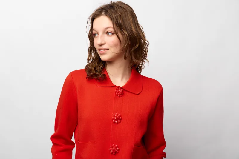 Young woman in red sweater looks to side with slight smile on white background. Casual style, natural expression, and simple studio portrait with soft lighting and relaxed mood.