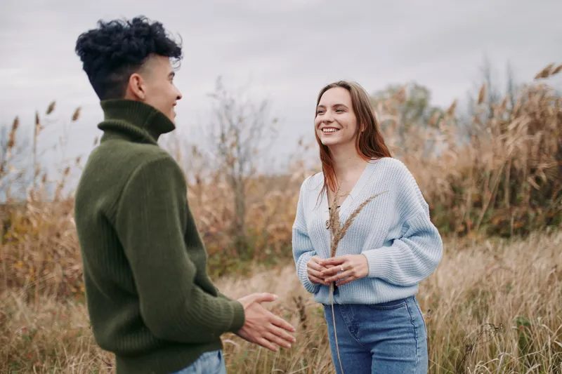 Two young people in a grassy field share a candid conversation, smiling and showing genuine connection and honest expressions that emphasize authenticity and natural relaxed body language.