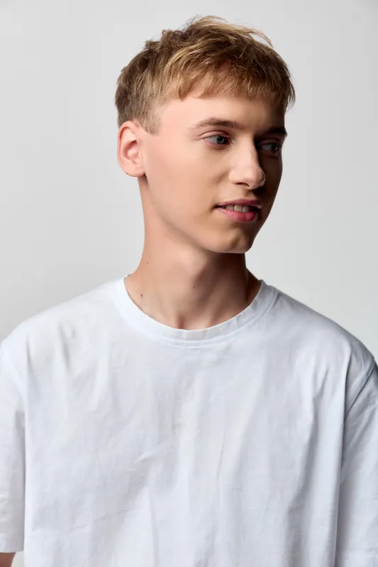 Young man in a white shirt, side profile against a neutral backdrop, casual fashion, studio lighting, clean minimal style, relaxed expression, suitable for stock imagery and modern campaigns