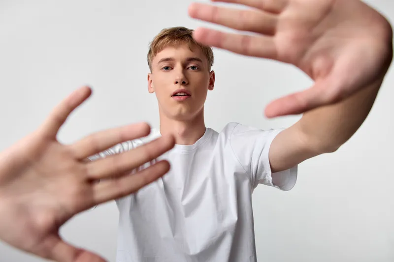 Man in white t shirt reaching toward the camera with hands in the foreground, dynamic perspective, motion and interaction captured in a bold studio shot