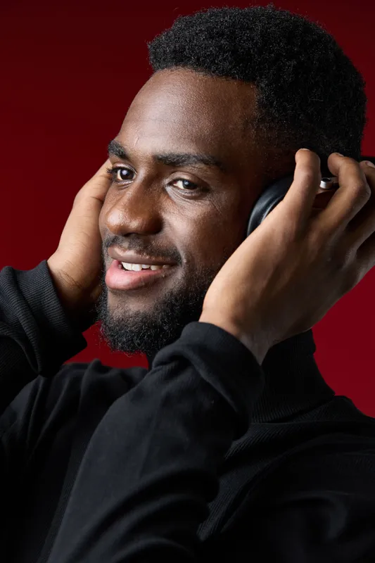 Happy young African man enjoying music with headphones against a vibrant red background, showcasing a joyful emotion and modern style