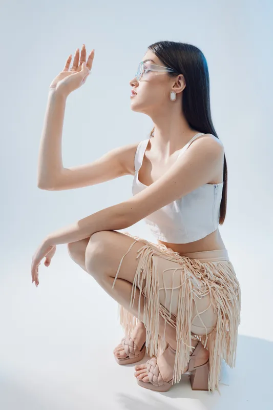 Elegant woman in trendy fashion outfit poses in studio with white background. Concept of beauty, style, and modern fashion with natural lighting and minimalistic setting.