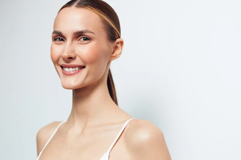 Woman smiling portrait beauty skincare young studio background relaxed closeup of fresh face with natural skin minimal makeup calm gaze soft light healthy feminine