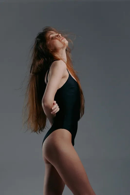 young woman in black bodysuit posing confidently with long hair on gray background