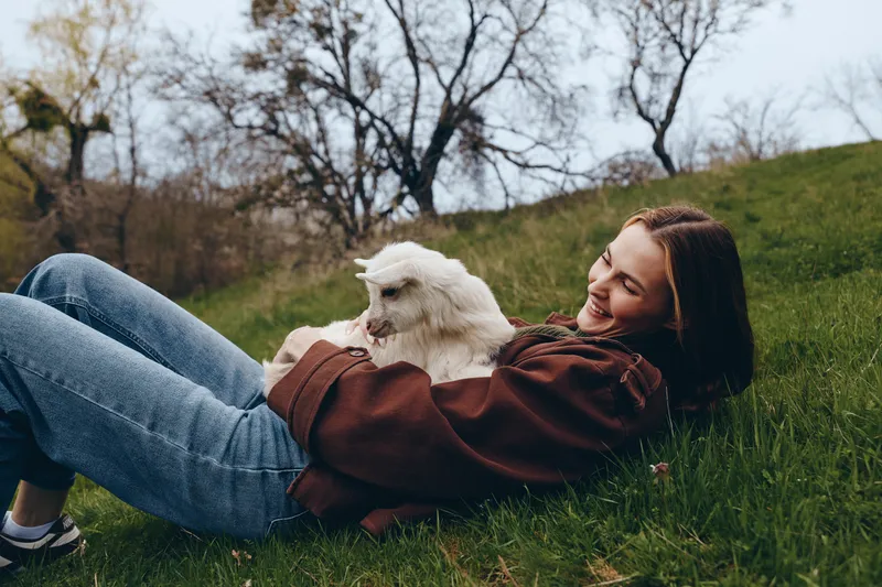 A relaxed woman lounges on grass with a small dog in an outdoors park, capturing a lifestyle moment of comfort and companionship, ideal for wellness, balance, and everyday joy.