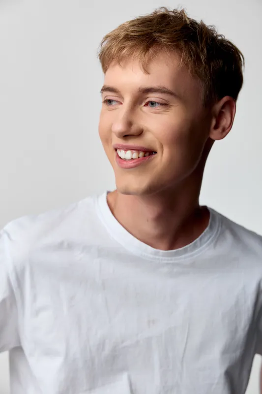 Smiling man in a white t shirt posed in a bright studio, conveying casual happiness, friendly demeanor and fresh energy suitable for lifestyle, fashion, and promotional uses.