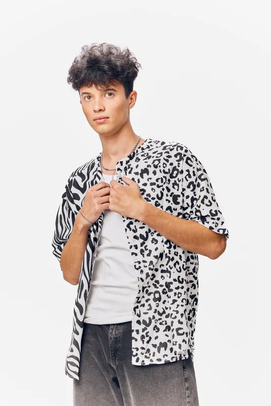 young man in patterned shirt with curly hair poses confidently against white background in casual style and modern fashion, showcasing relaxed yet trendy vibe