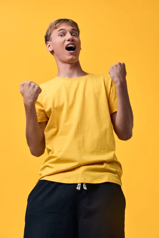 Excited man in a yellow t shirt raises fists in celebration, capturing vibrant energy and triumphant emotion in a bold casual pose. Vibrant, motivating vibe.