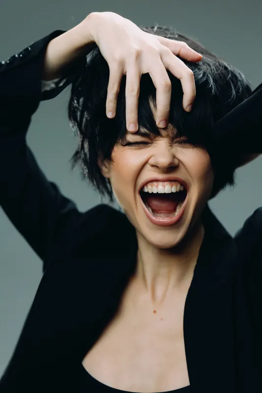 expressive woman screaming with hand in hair showing strong emotion and black outfit