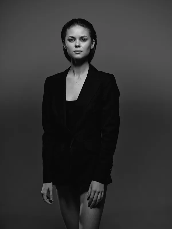 Black and white portrait of a serious woman in a black blazer with minimal makeup and slicked-back hair.