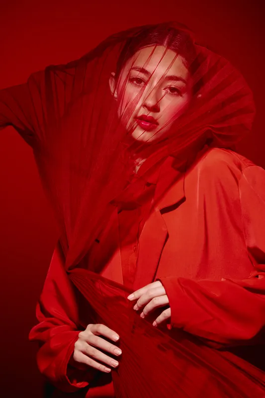 Creative beauty portrait of a woman in intense reds with elegant sheer fabric. High fashion editorial look suitable for artistic and beauty concepts.
