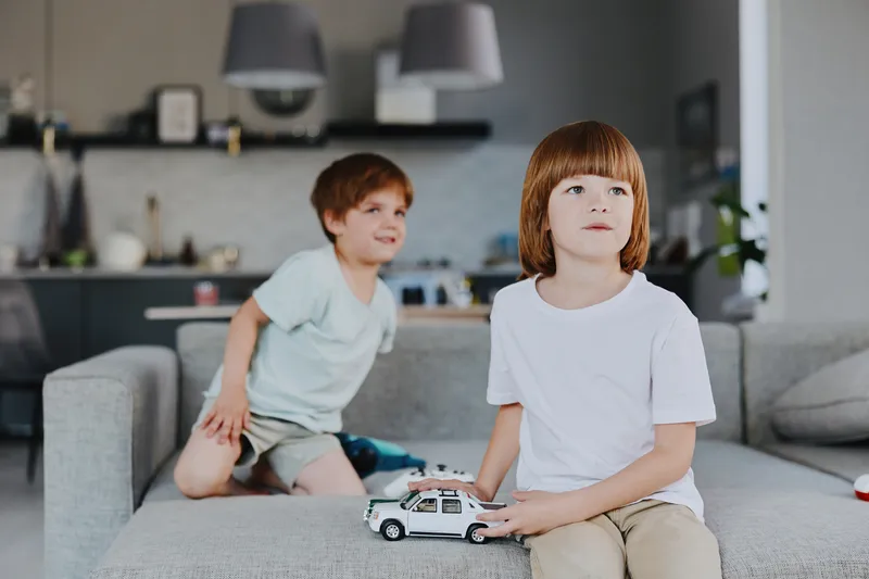 Two boys playing with toy cars in a modern living room, expressing joy and creativity, surrounded by a stylish interior design rich in natural light.