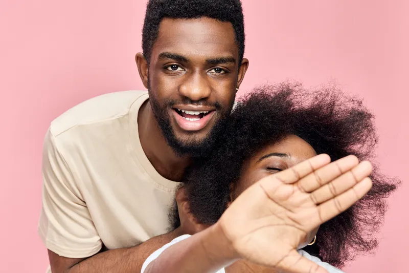 Happy couple with natural afro hair enjoying playful moment on pink background, showcasing love, joy, and intimacy, perfect for relationship themes and lifestyle projects
