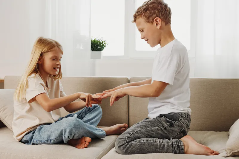 Happy boy and girl play together on sofa indoors, smiling and enjoying family time in bright living room. Concept of childhood, sibling bonding, and home happiness.