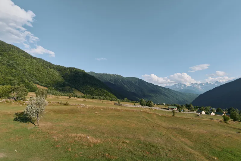 A serene valley landscape with rolling meadows and distant hills under a clear blue sky, inviting calm and outdoor exploration in a wide natural setting.