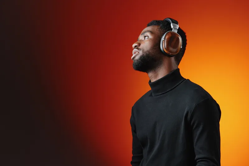 A young Black man enjoying music with stylish headphones, showcasing a relaxed expression against a vibrant orange gradient background