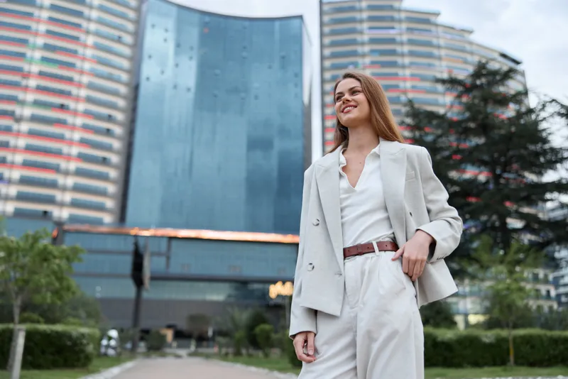 confident woman in white business suit walking outdoors with modern cityscape background smiling positive