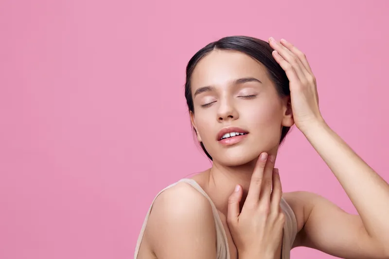 Young woman with closed eyes, soft skin, and gentle smile poses against a pink background, embodying beauty, tranquility, and inner peace ideal for skincare and beauty themes