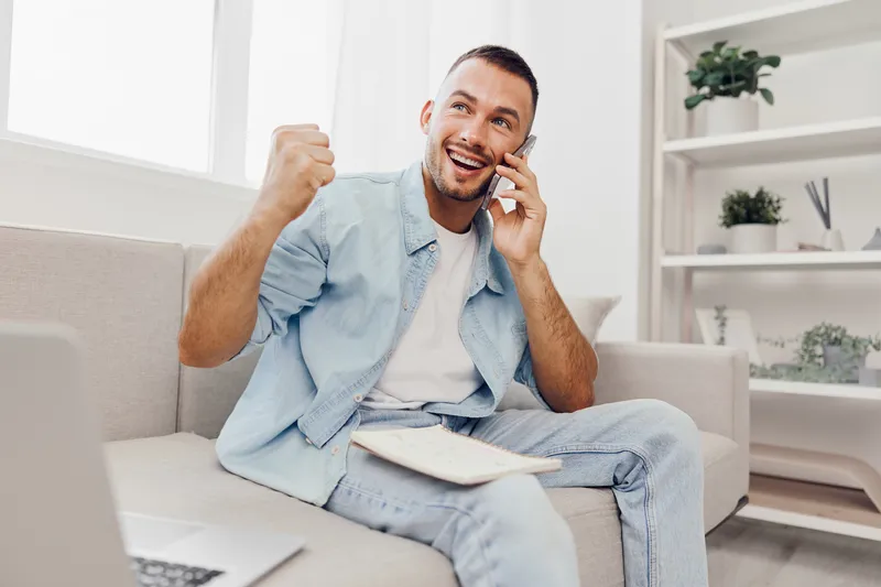 Excited man celebrating success while on the phone, casual style, bright setting, contemporary decor, showcasing happiness and achievement.