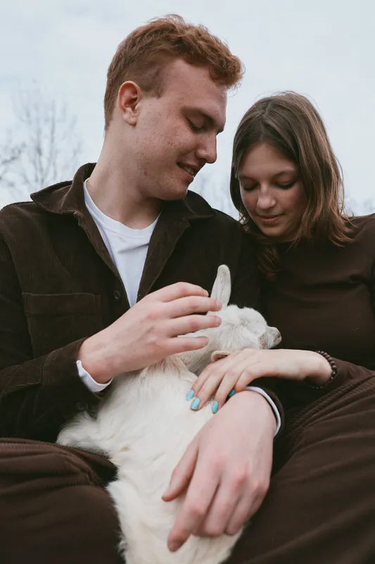 A couple share a quiet moment outdoors, cradling a small animal in their arms. They smile softly as the creature rests against them, symbolizing warmth, connection, and simple joys of family life,