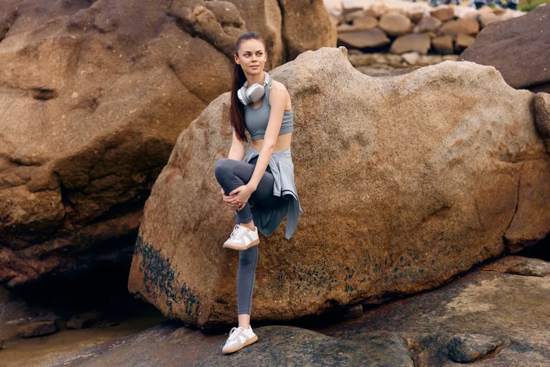 Fitness model in activewear posing on a rock, showcasing healthy lifestyle and athletic wear, with a serene nature background featuring rocks and greenery