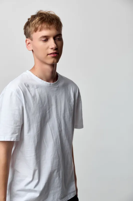 Young man in a white t shirt in a neutral studio, casual style and simplicity, clean composition with soft lighting for fashion or lifestyle stock use