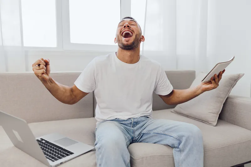 Happy man enjoying solo living and digital detox at home, celebrating personal achievements while balancing work-life blur and mental health.