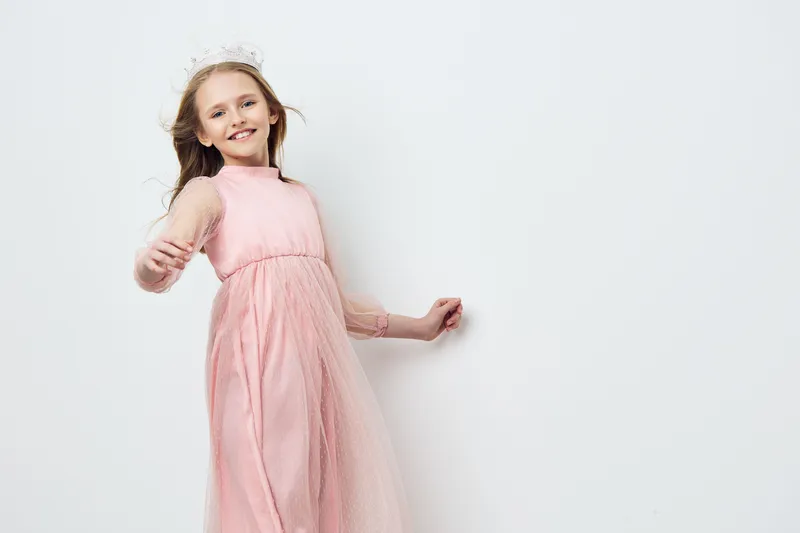 Happy young girl smiling in a pink dress, conveying joy and innocence against a light background, perfect for children s fashion and celebrations