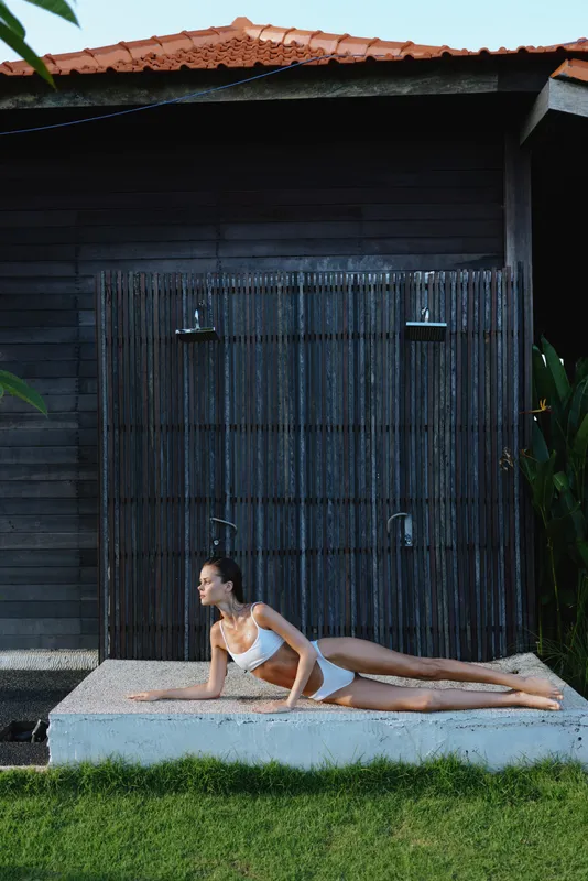 A woman performs a cobra yoga pose on a raised outdoor platform, sunlight on green grass, a wooden shed in the background, lifestyle image highlighting fitness, balance and serenity in a backyard.