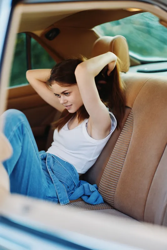 Young woman in casual outfit relaxing in vintage car interior, expressing joy and freedom. Sunlight streaming in, creating a vibrant, uplifting atmosphere.