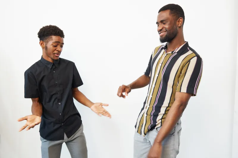 Two black men enjoying a lively moment, showcasing joy and connection, dressed casually in stylish clothing. Their cheerful expressions capture a vibrant atmosphere.