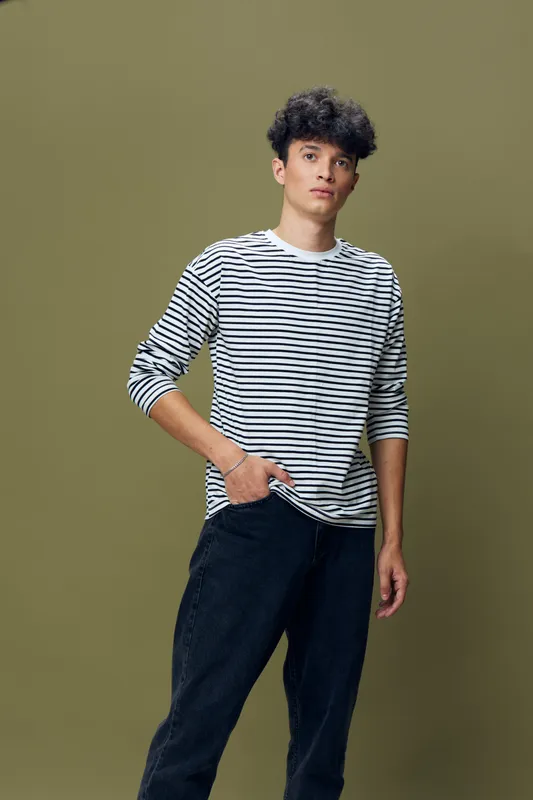 young man in striped shirt standing confidently with casual dark pants against olive background, natural pose, relaxed expression, studio lighting