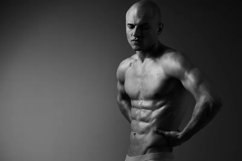 Muscular man posing in a dramatic black and white scene, showcasing strength and determination with a powerful expression and artistic lighting.