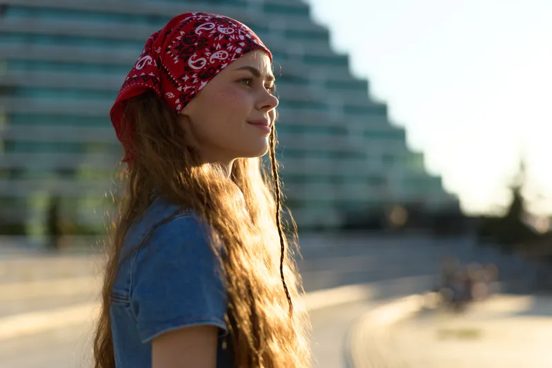 lifestyle woman with long hair in modern boho-western denim street style wearing red bandana, warm film color, casual outdoor urban fashion portrait, natural sunlight