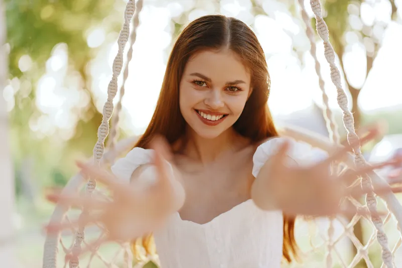 Young woman smiling joyfully in a swing against a natural background, embodying happiness and carefree spirit during summer, with bright colors and warm light