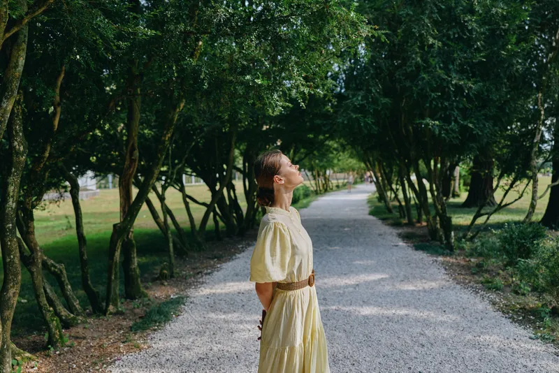 woman outdoors park portrait with yellow dress on a gravel path in a lush environment serene sunlight textures and greenery under trees creating a peaceful summer mood