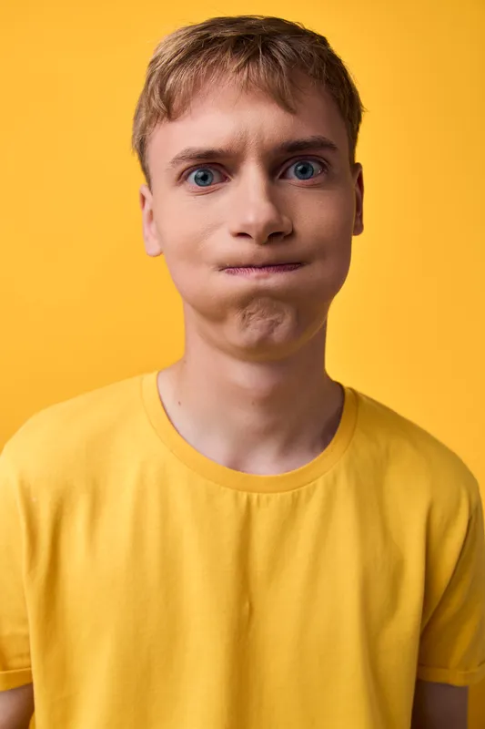 Child with a funny face wearing a yellow shirt, closeup shot for playful mood and humorous expression, bright studio lighting and bold background enhance the cheeky character.