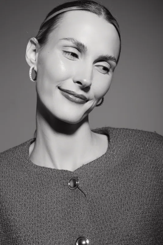 Close-up portrait of a white woman with light skin and slicked back hair smiling gently in studio. Concept of natural beauty, elegance, and soft mood in fashion photography.