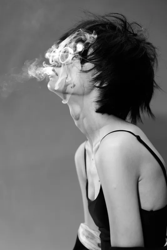 Black and white portrait of a woman exhaling smoke with rings, edgy style, moody atmosphere, expressive emotion.