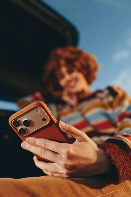 Woman lifestyle at home indoors, smartphone in hands on couch beneath blanket, warm evening light, casual leisure, relaxed posture, communication and browsing on screen, blurred cozy knit sweater