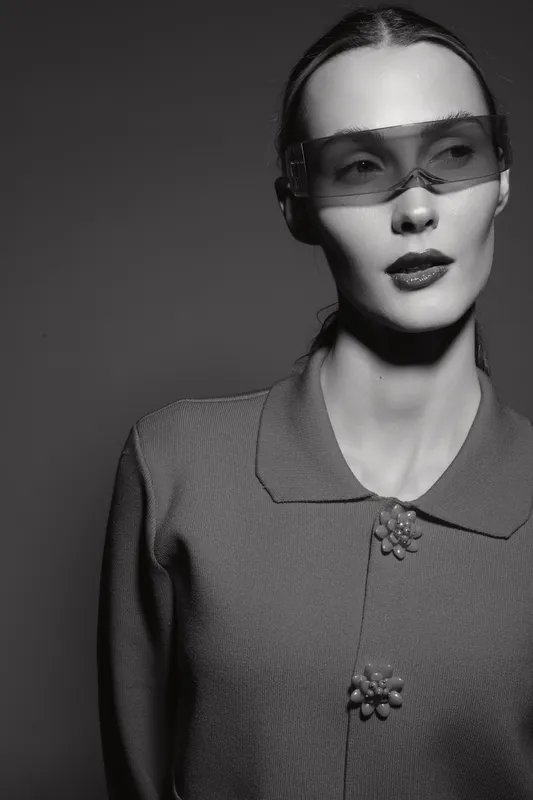 Portrait of a fair skinned Caucasian woman in futuristic glasses and textured jacket posing in studio with black background.