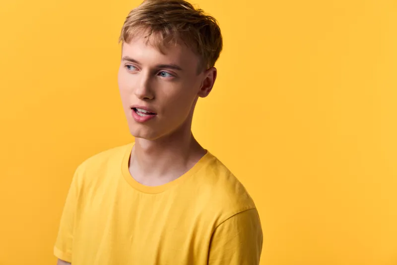 Young man yellow shirt studio expression casual warm background fashion, this relaxed pose captures a bright and thoughtful moment in a minimal setting with soft lighting and clean color tones.