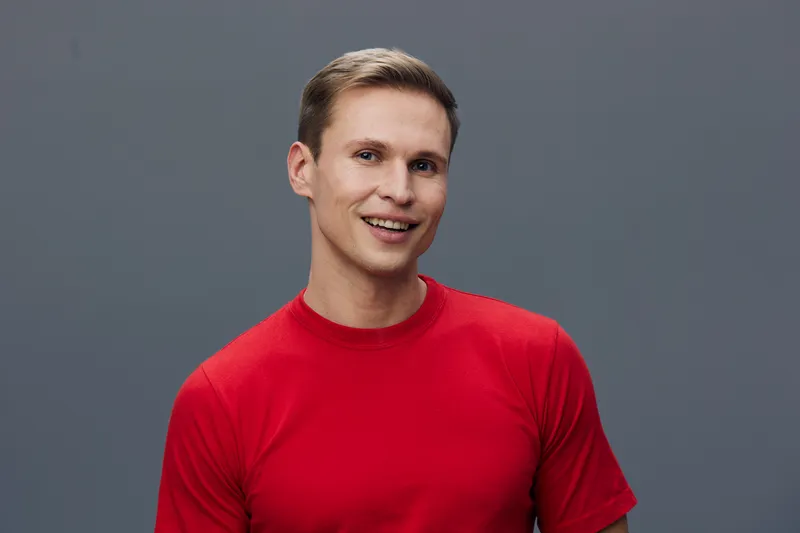Smiling young caucasian man wear red t-shirt look camera happy positive emotion digital nomad concept working with laptop communication modern casual style grey background