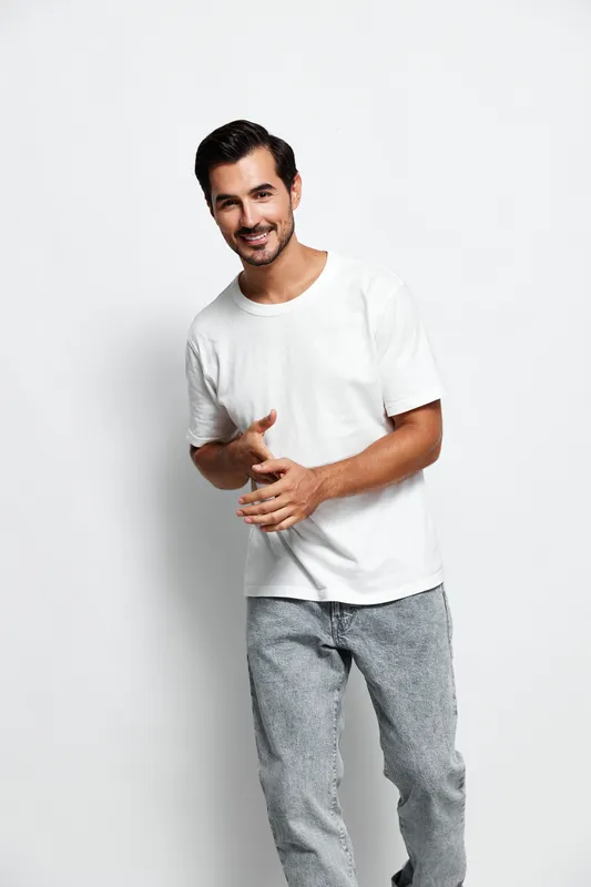 Full body smiling young man wearing a white t-shirt and gray pants, looking at the camera with a cheerful expression isolated on plain solid background. Lifestyle concept.