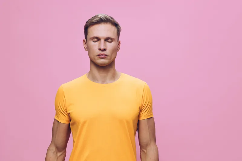 young man meditating with closed eyes wear orange t-shirt isolated on pink background wellness mental health concept mindfulness relaxation calmness