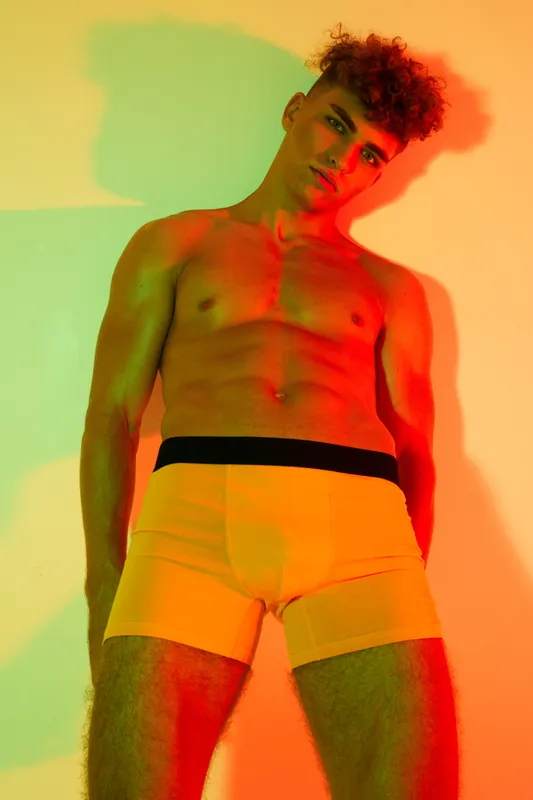 Man with muscular body posing in underwear, colored lights highlighting muscles, minimalistic background ready for fitness or fashion theme photography in studio setting.